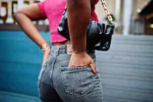 Photo gratuite jeune femme afro-américaine urbaine en haut rose et jeans gris avec sac à main afro fashion chic femmes dos fesses