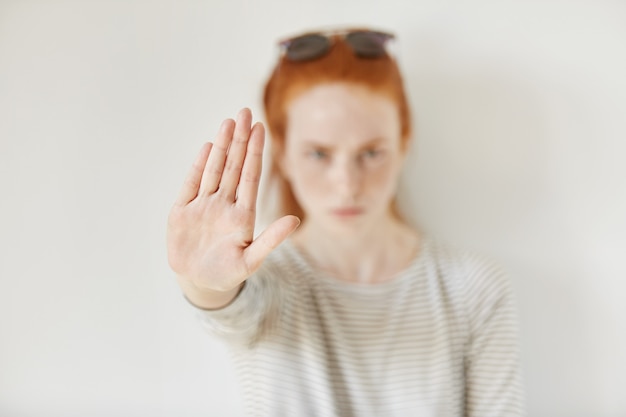 Jeune femme agacée avec une mauvaise attitude faisant un geste d'arrêt avec sa paume vers l'extérieur, disant non, exprimant un refus ou une restriction. Émotions humaines négatives, sentiments, langage corporel. Mise au point sélective à portée de main