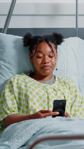 Jeune femme agitant la caméra d'appel vidéo sur smartphone pour parler à ses amis et à sa famille au lit. Patient atteint d'une maladie utilisant une conférence à distance en ligne sur un téléphone portable dans la salle d'hôpital.