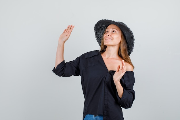 Photo gratuite jeune femme en agitant les mains tout en regardant en chemise, short, chapeau et à la joyeuse