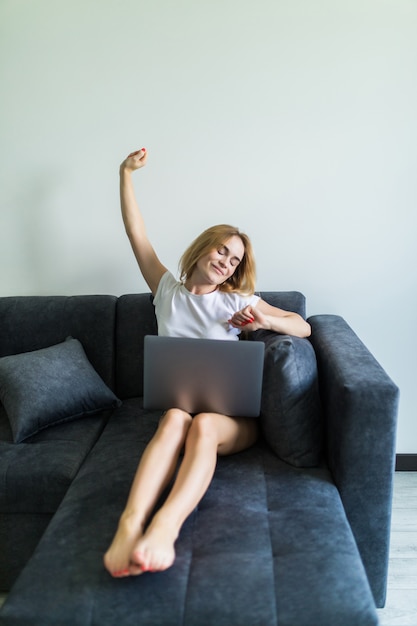 Jeune femme à l'aide d'un ordinateur portable tout en levant la main et assis sur le canapé à la maison