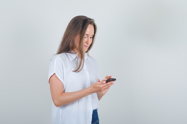 Jeune femme à l'aide de téléphone portable en t-shirt, jeans et à occupé