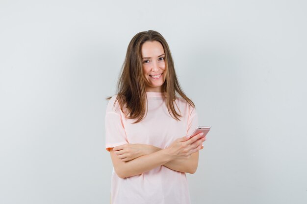 Jeune femme à l'aide de téléphone portable en t-shirt rose et à la bonne humeur. vue de face.