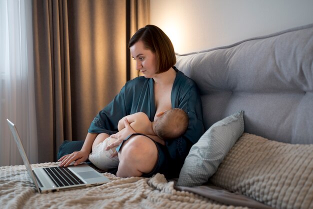 Jeune femme allaitant son bébé mignon tout en travaillant