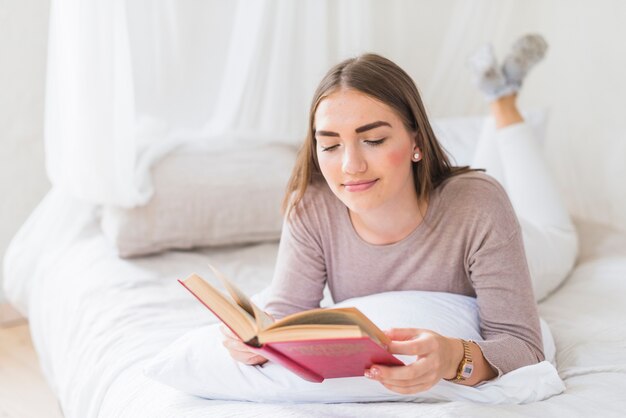 Jeune femme allongée sur le lit, appréciant le livre de lecture