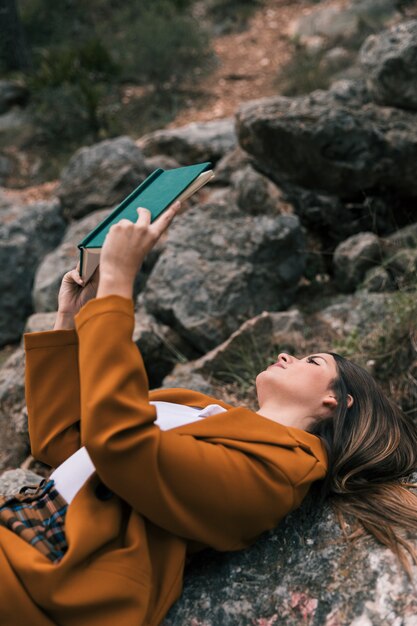 Jeune femme allongée sur un rocher en lisant le livre