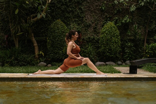 Jeune femme à l'apparence positive du corps pratiquant le yoga seule sur le pont au bord de la piscine de l'île tropicale de Bali, en Indonésie. Sport, fitness, concept de mode de vie sain.