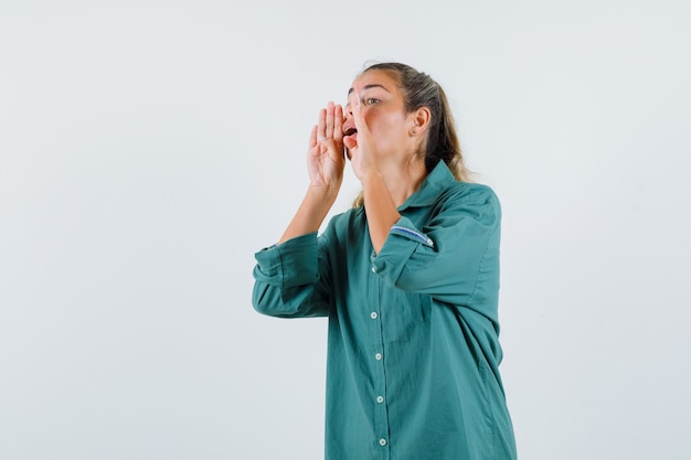 Jeune femme appelant quelqu'un avec une voix forte en chemise bleue et à la recherche d'impuissance