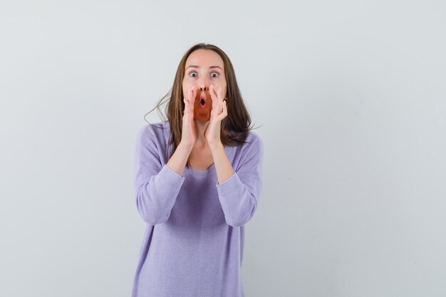 Jeune femme appelant quelqu'un avec une voix forte en chemisier lilas et à la recherche concentrée