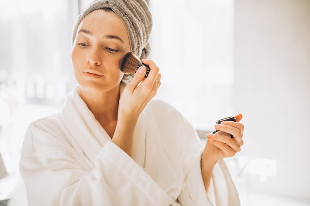 Jeune femme appliquant le blush et regardant dans le miroir