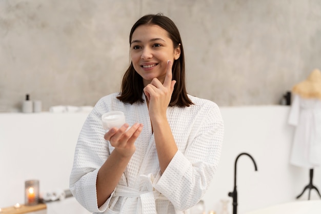 Jeune femme appliquant une crème hydratante sur son visage avant de prendre un bain