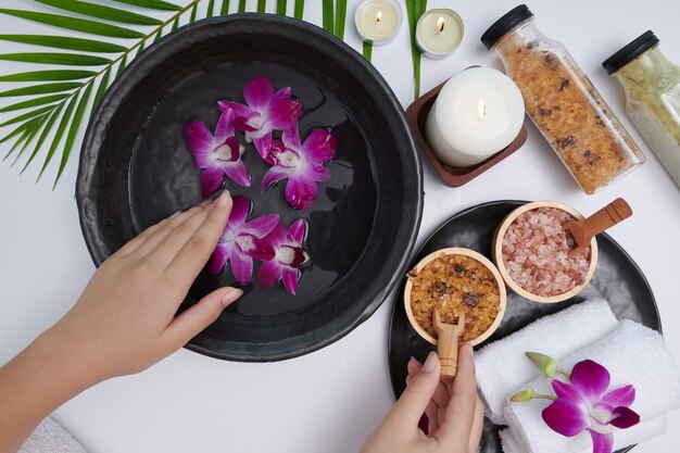 Jeune femme appliquant un gommage naturel sur les mains contre une surface blanche. Cure thermale et produit pour le spa des mains féminines, massage, eau de fleurs parfumées et bougies, Détente. Mise à plat. vue de dessus.