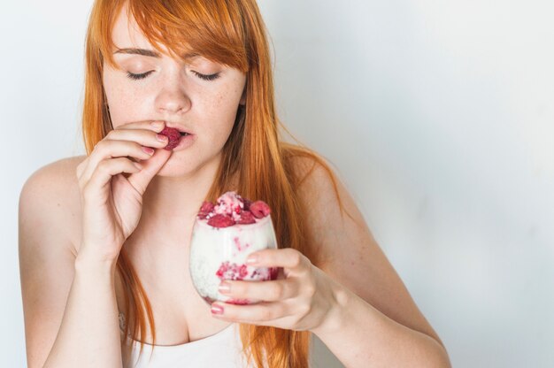 Jeune femme appréciant les framboises en smoothie au yaourt sur fond blanc