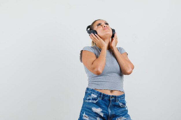 Jeune femme appréciant la musique avec des écouteurs en t-shirt, short et à la ravie.