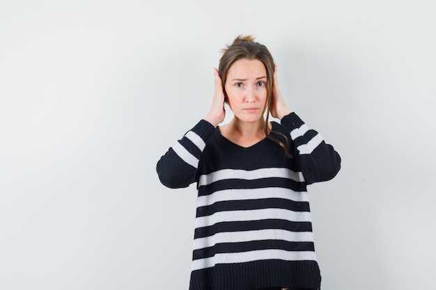 Jeune femme en appuyant sur les mains sur les oreilles en chemisier noir et pantalon noir et à l'ennui