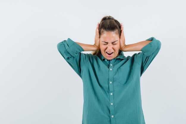 Jeune femme en appuyant sur les mains sur les oreilles en chemisier vert et à la hâte