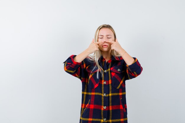 Jeune femme en appuyant sur le nez avec les doigts en chemise à carreaux et à la vue de face, focalisée.