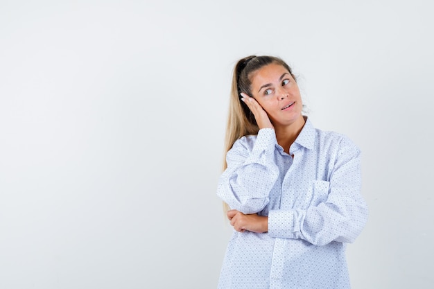 Jeune femme appuyée sur la joue sur la paume, regardant le côté gauche en chemise blanche et à heureux