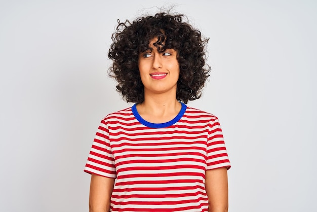 Photo gratuite jeune femme arabe aux cheveux bouclés portant un t-shirt rayé sur fond blanc isolé souriant regardant sur le côté et regardant loin en pensant