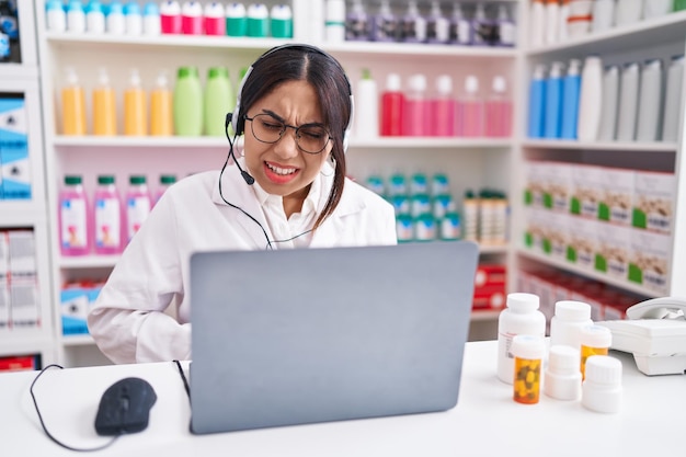 Jeune femme arabe travaillant à la pharmacie à l'aide d'un ordinateur portable avec la main sur le ventre parce que l'indigestion, la maladie douloureuse se sent mal. notion de mal.