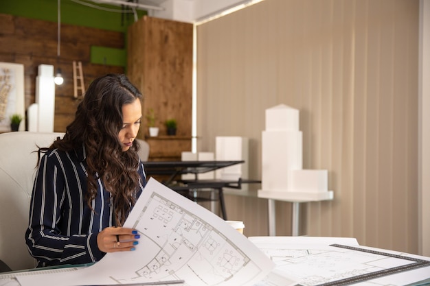 Jeune femme architecte qui contrôle les esquisses du projet immobilier. Lieu de travail confortable