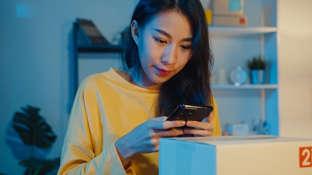 Jeune femme asiatique à l'aide de smartphone prenant photo de code à barres sur le produit de colis pour la livraison au client