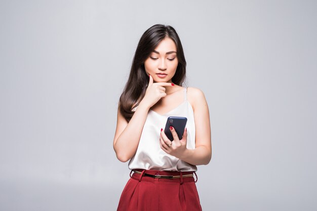 Jeune femme asiatique à l'aide d'un téléphone intelligent isolé sur mur blanc.