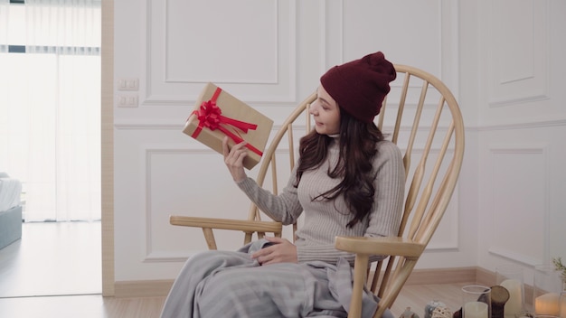 Jeune femme asiatique assise sur une chaise enveloppée dans une couverture grise dans son salon à la maison.