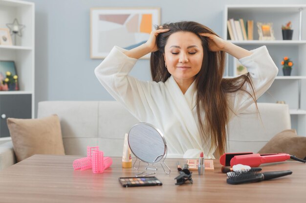 Jeune femme asiatique aux cheveux longs noirs assis à la coiffeuse à la maison faisant un massage du cuir chevelu relaxant faisant la routine de maquillage du matin