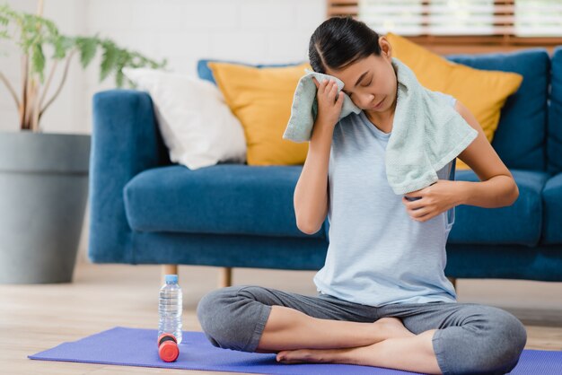 Jeune femme asiatique buvant de l&#39;eau parce qu&#39;elle se sent épuisée au repos après l&#39;exercice dans le salon