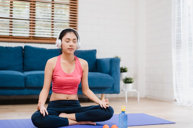 Jeune femme asiatique écoute de la musique tout en pratiquant le yoga dans le salon