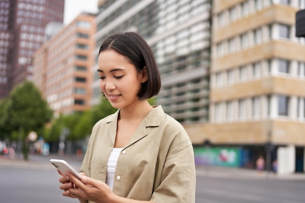 Jeune femme asiatique explorant la ville avec une application pour smartphone tenant un téléphone portable et marchant discrètement