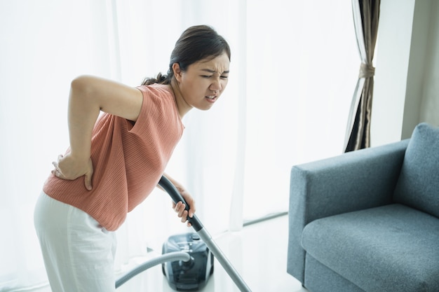 Une jeune femme asiatique a mal au dos après avoir fait des travaux ménagers pendant un certain temps, la femme de ménage a un problème physique à cause du travail acharné. une femme au foyer s'est blessée au dos à cause d'un grave problème de santé.