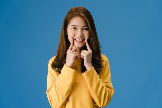 Jeune femme asiatique montrant le sourire, l'expression positive, vêtue d'un tissu décontracté et regarde la caméra isolée sur fond bleu. Heureuse adorable femme heureuse se réjouit du succès. Concept d'expression faciale.