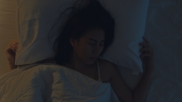 Jeune femme asiatique nerveuse ayant un cauchemar allongée sur un lit dans sa chambre à la maison en pleine nuit. Souffrant de maux de tête ou de migraine, d'insomnie, d'apnée du sommeil ou de stress. Vue de dessus