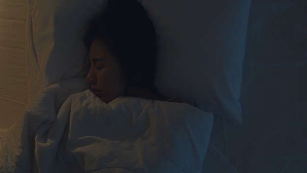 Jeune femme asiatique nerveuse ayant un cauchemar allongée sur un lit dans sa chambre à la maison en pleine nuit. Souffrant de maux de tête ou de migraine, d'insomnie, d'apnée du sommeil ou de stress. Vue de dessus