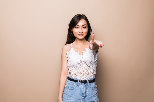 Jeune femme asiatique pointant vous isolé sur mur beige.