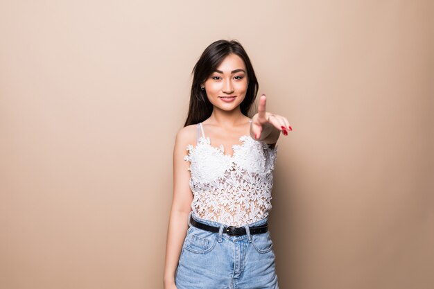 Jeune femme asiatique pointant vous isolé sur mur beige.