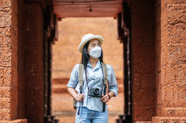 Jeune femme asiatique portant un chapeau et un masque de protection lors d'un voyage dans un site historique