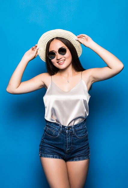 Jeune femme asiatique avec surprise pose isolé sur fond bleu. Portrait de la belle femme asiatique en chapeau de paille et lunettes de soleil sur fond bleu