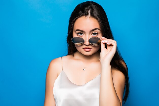 Jeune femme asiatique avec surprise pose isolé sur fond bleu. Portrait de la belle femme asiatique en chapeau de paille et lunettes de soleil sur fond bleu