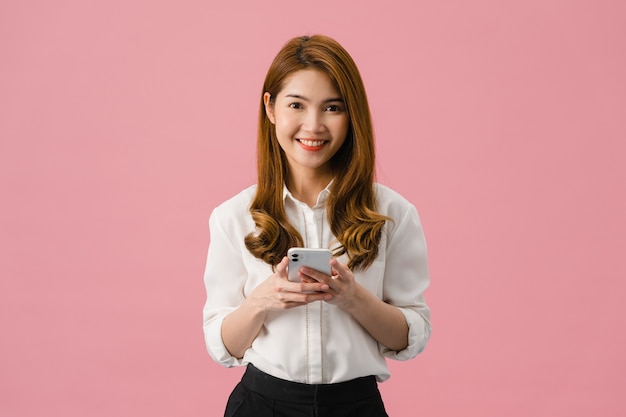 Une Jeune Femme Asiatique Surprise Utilisant Un Téléphone Portable Avec Une Expression Positive, Sourit Largement, Vêtue De Vêtements Décontractés Et Regarde La Caméra Sur Fond Rose.