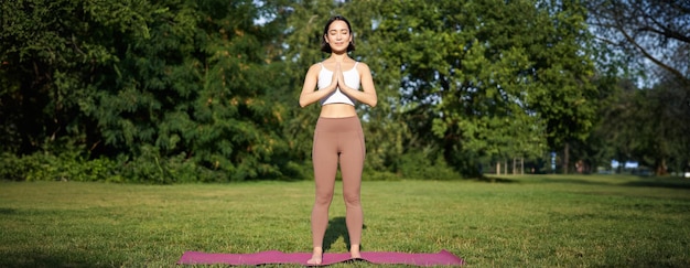 Photo gratuite jeune femme asiatique en vêtements de sport se tenant la main dans le geste du namaste pratiquant le yoga méditant et