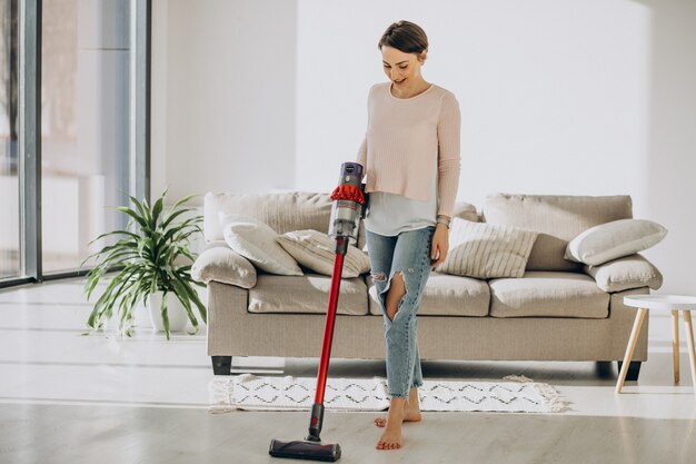 Jeune femme avec un aspirateur rechargeable nettoyant à la maison