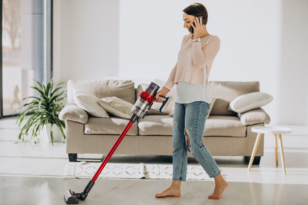 Jeune femme avec un aspirateur rechargeable nettoyant à la maison