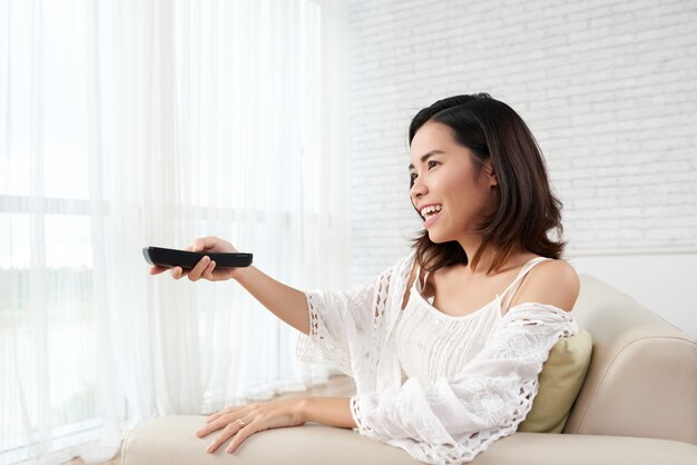 Jeune femme assise sur un canapé à la maison allumer la télévision