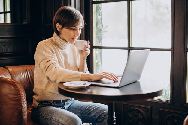 Jeune femme assise dans un café buvant du café et travaillant sur un ordinateur