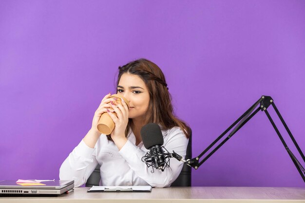 Jeune femme assise derrière le bureau et buvant du café Photo de haute qualité