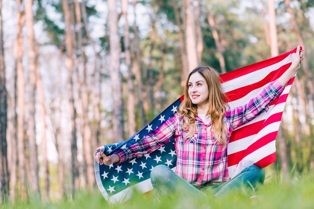 Jeune femme assise sur l&#39;herbe et tenant le drapeau américain