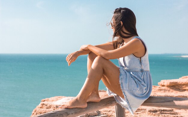 Jeune femme assise sur une planche et regardant la mer pendant la journée
